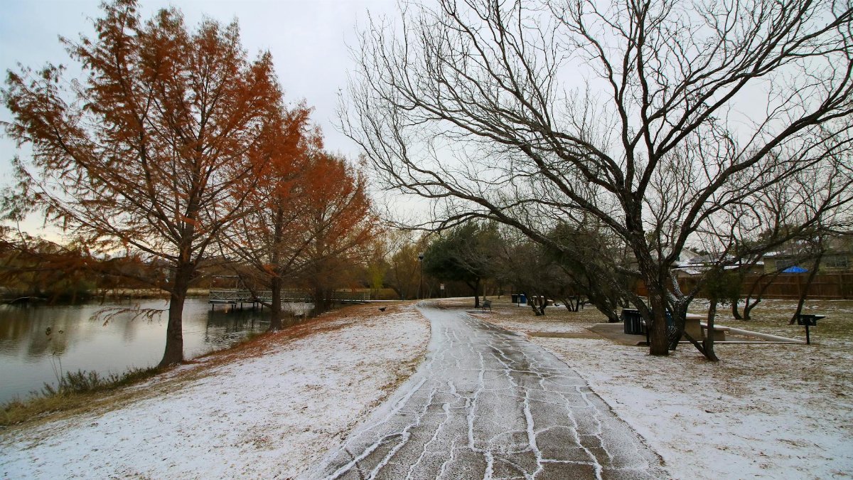 A tranquil winter scene in San Antonio, Texas, showcasing a snow-covered path lined with trees beside a serene lake.
