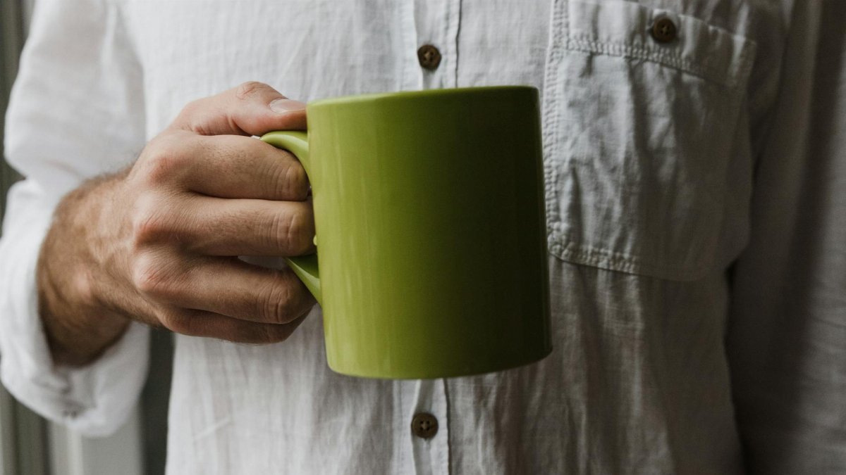 A man holding a green mug close-up wearing a white shirt, indoors setting.