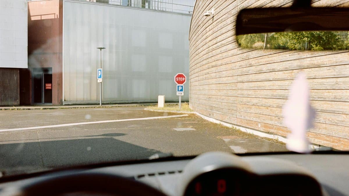 View from inside a parked car at a street intersection with stop and parking signs visible.
