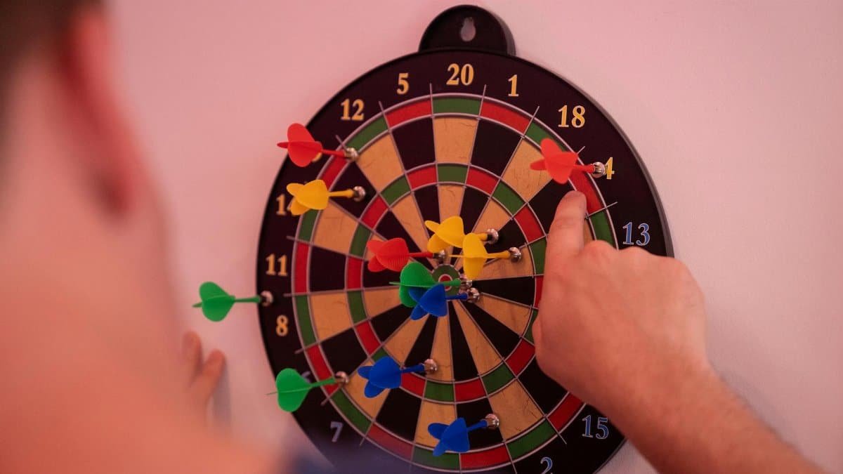 Hand pointing at colorful darts on a dartboard, highlighting accuracy and focus.