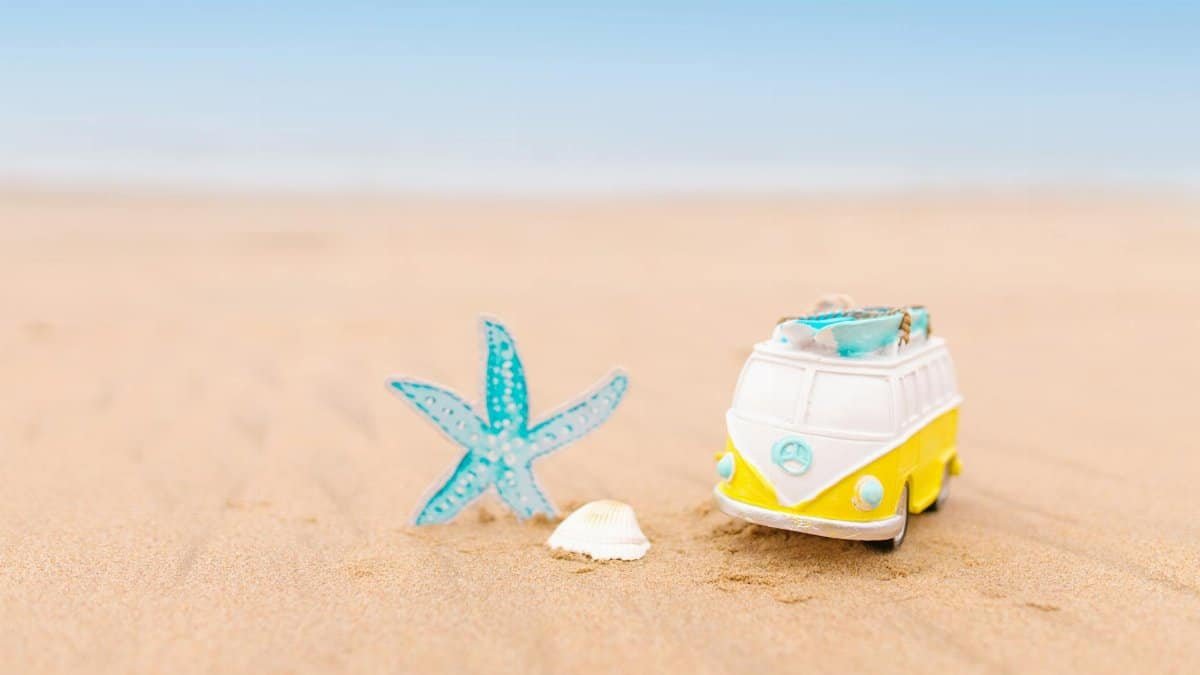 A toy van and starfish on a sandy beach under a clear blue sky, evoking summer vibes.