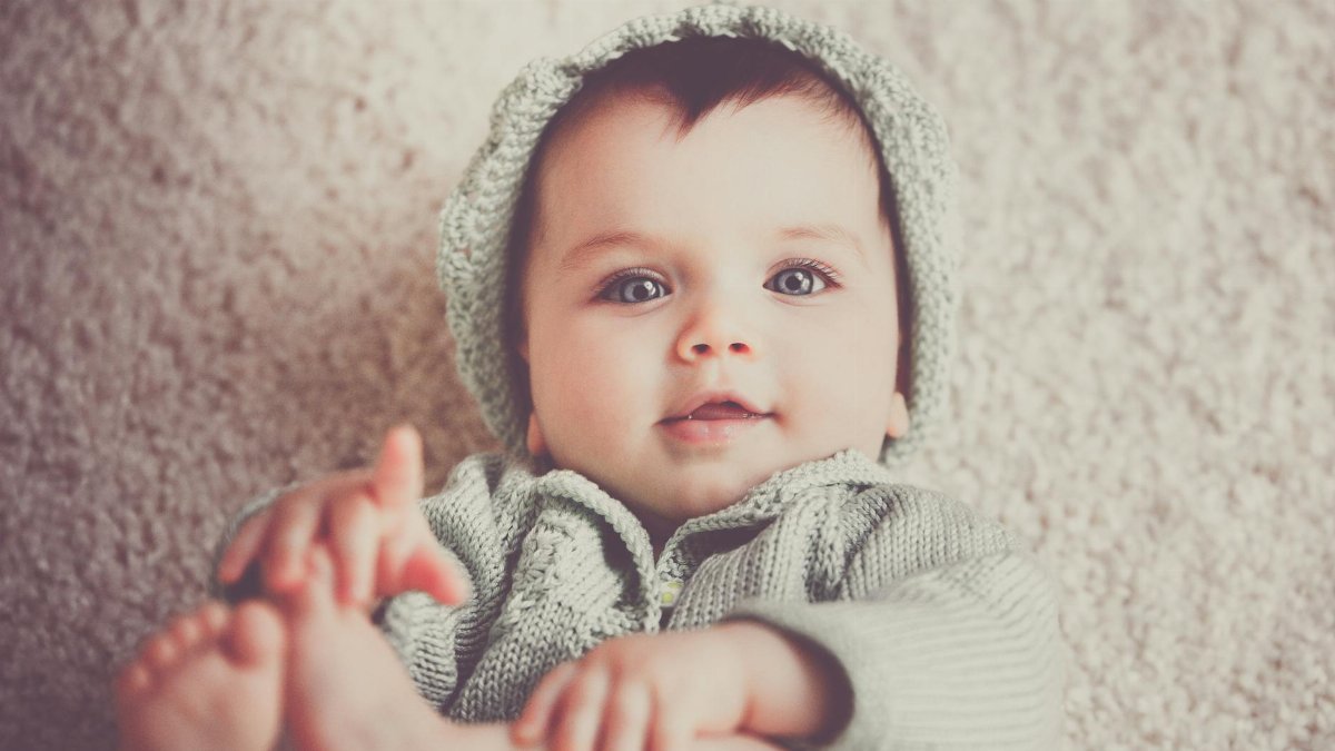 A cute baby in a knitted outfit lying on a soft carpet, smiling warmly.