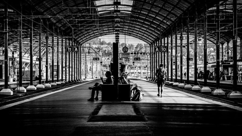Monochrome image of a railway station with people waiting and walking.
