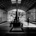 Monochrome image of a railway station with people waiting and walking.