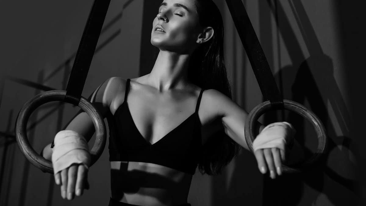 Black and white photo of a woman gymnast using rings, highlighting elegance and strength.