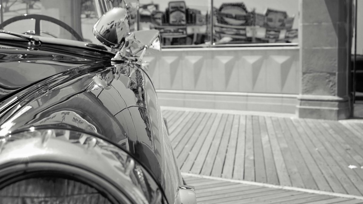 Black and white photo of a vintage car on the Atlantic City boardwalk, reflecting urban scenery.