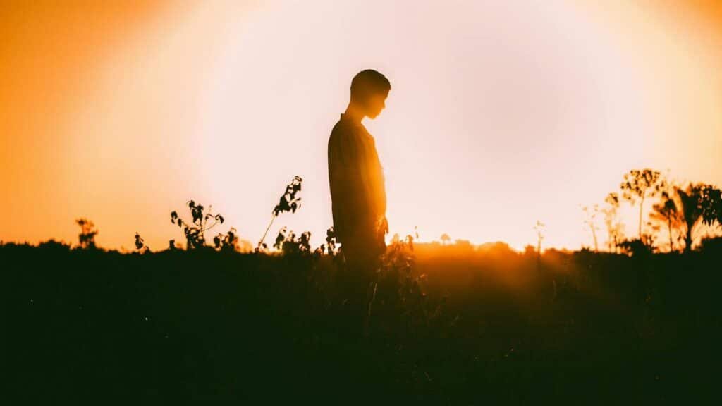 A captivating silhouette of a person standing in a field against a vibrant sunset backdrop.