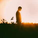 A captivating silhouette of a person standing in a field against a vibrant sunset backdrop.