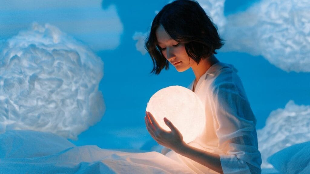 A woman in a dream-like setting holding a glowing sphere surrounded by cloud-like formations.