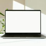 A sleek laptop with a white screen on a desk with green plants in the background.