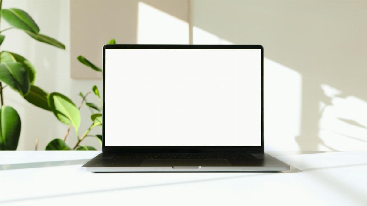 A sleek laptop with a white screen on a desk with green plants in the background.
