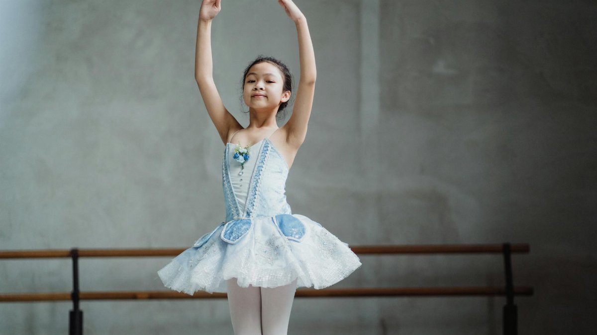A child ballerina in a tutu performs ballet moves in a dance studio.