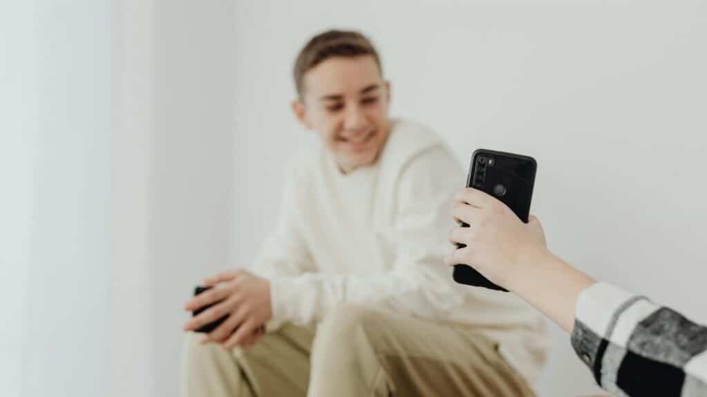 Teen boy smiling while chatting with a friend via smartphone indoors.