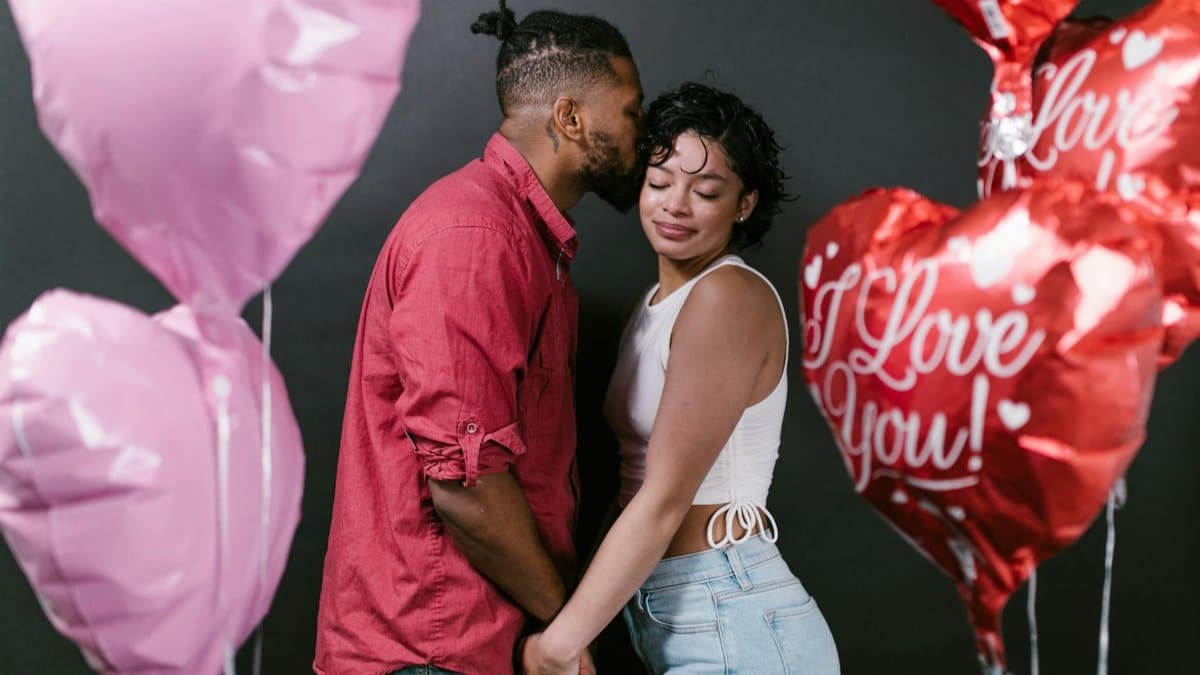 Romantic couple holding hands surrounded by heart-shaped balloons, celebrating love.