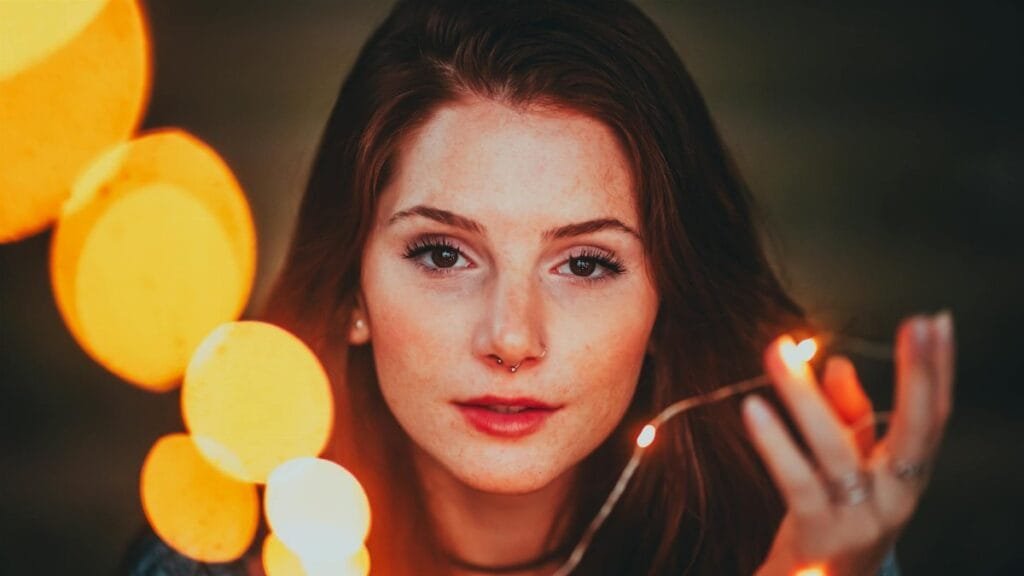 Artistic close-up portrait of a woman with glowing string lights creating a magical effect.