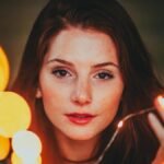 Artistic close-up portrait of a woman with glowing string lights creating a magical effect.