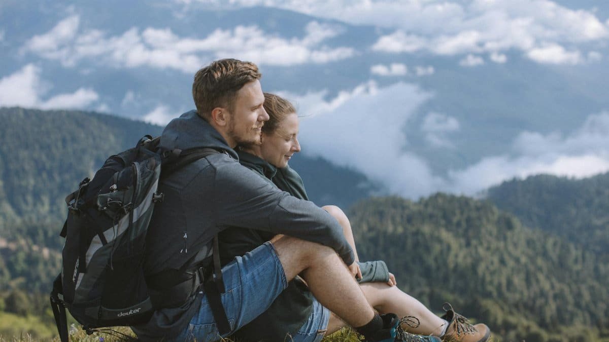 A happy couple sitting and embracing while enjoying a scenic mountain view during a hiking adventure.
