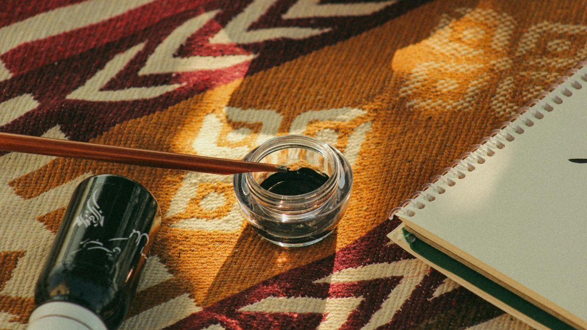 A creative flat lay featuring an ink bottle, brush, and notepad on a patterned fabric.