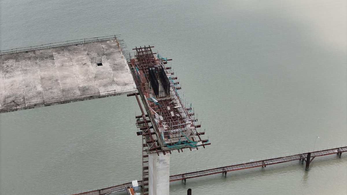 Aerial view of an unfinished bridge structure over water, showcasing construction progress.