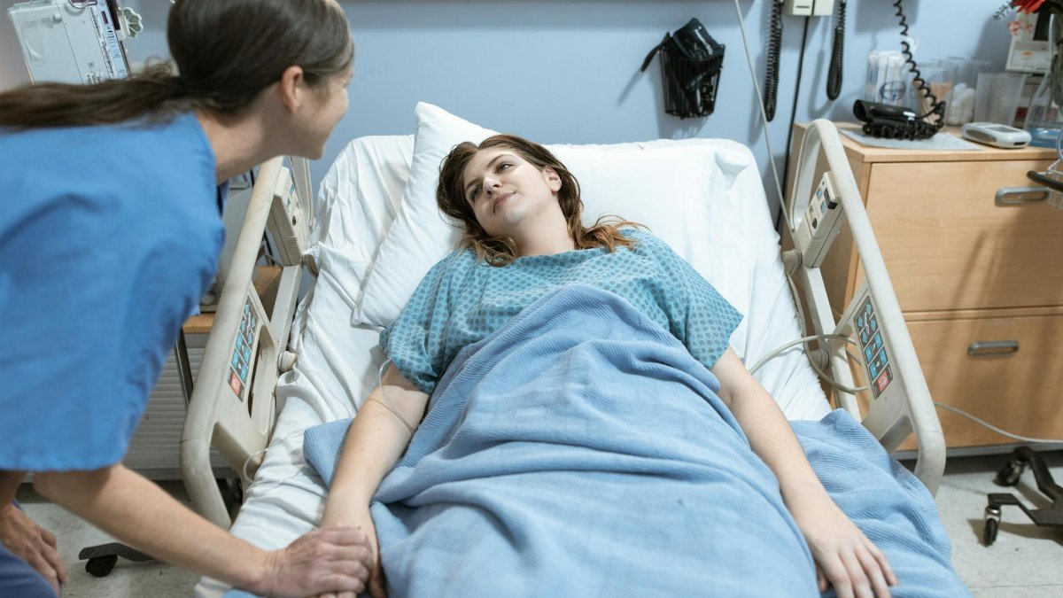 A nurse compassionately holds a patient's hand in a hospital room setting, promoting care and support.