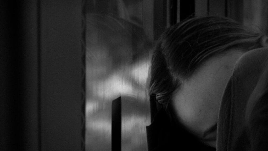 A person resting their head on a train window, captured in black and white, evokes a serene and reflective mood.