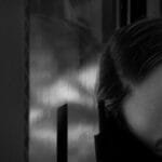 A person resting their head on a train window, captured in black and white, evokes a serene and reflective mood.