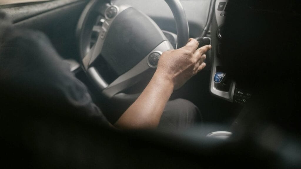 High angle of crop unrecognizable male driving modern car on street on sunny day