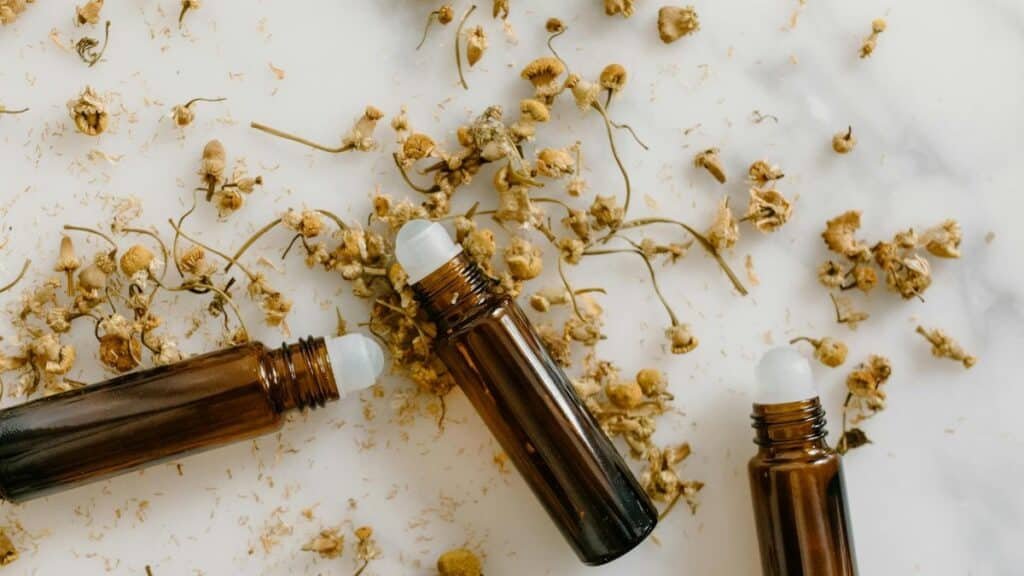Brown roll-on bottles with dried chamomile flowers on a white background.