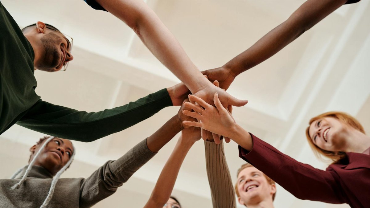 A diverse group of young adults forming a united circle with hands together indoors.