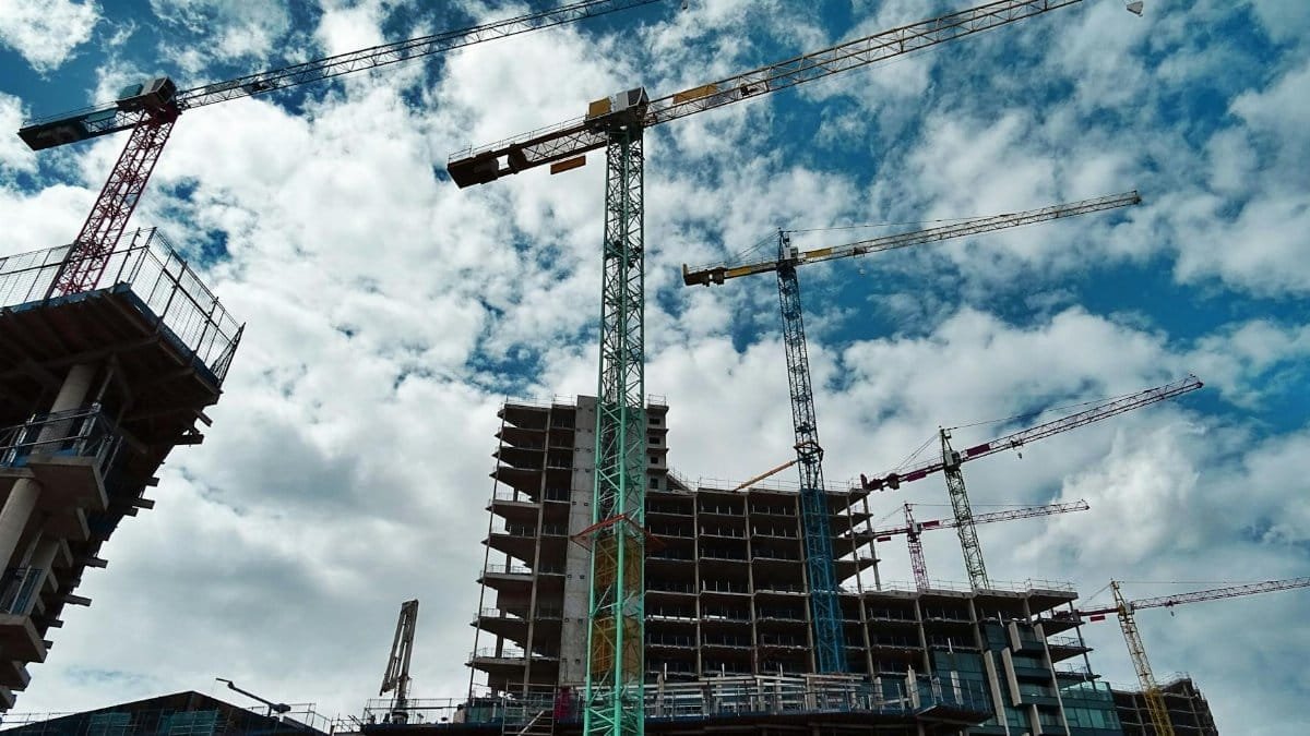 Urban construction site with numerous cranes framing rising skyscrapers against a blue sky.
