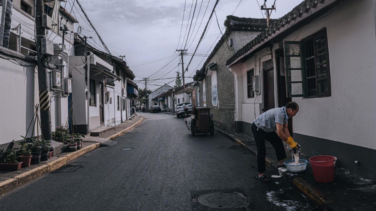 Man cleaning fish on a peaceful residential street in an East Asian neighborhood.