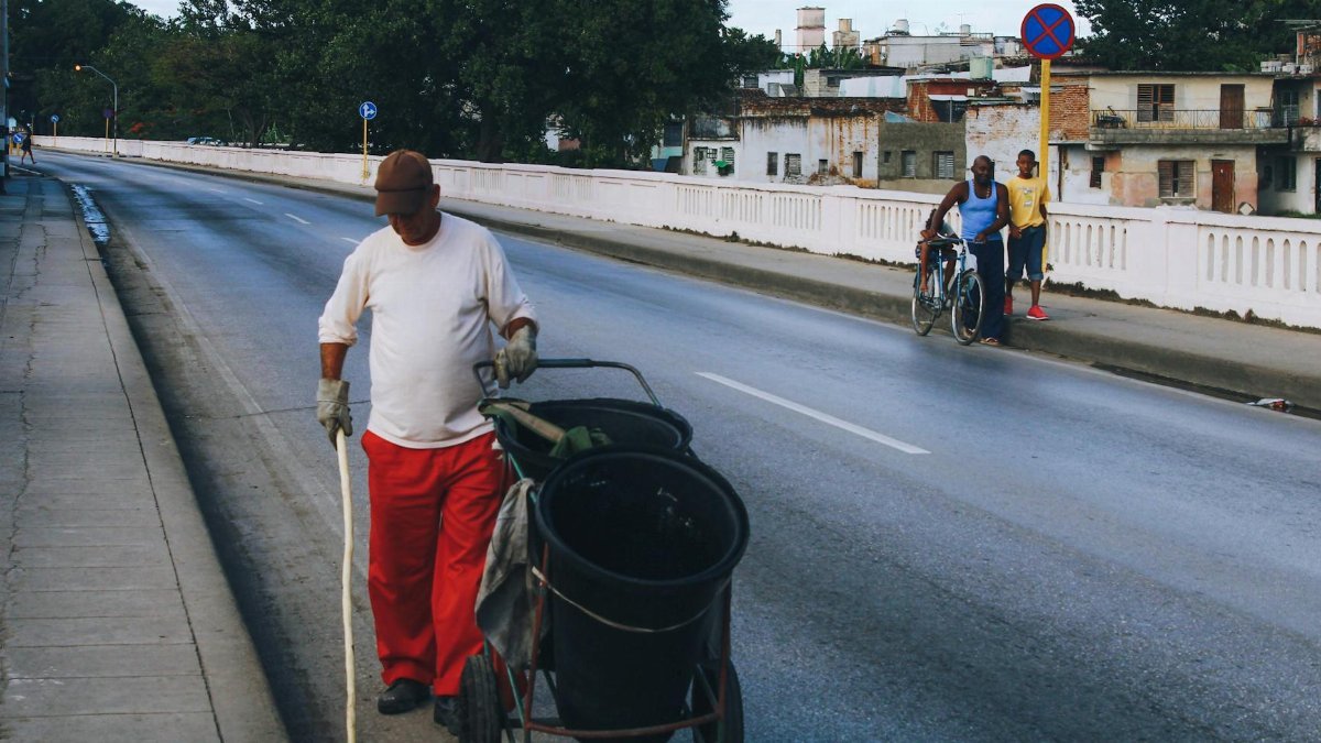 Man cleaning a city sidewalk with a pushcart, illustrating urban maintenance.