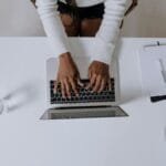 Top view of a woman typing on a laptop at a modern, minimalist home office desk with plants.