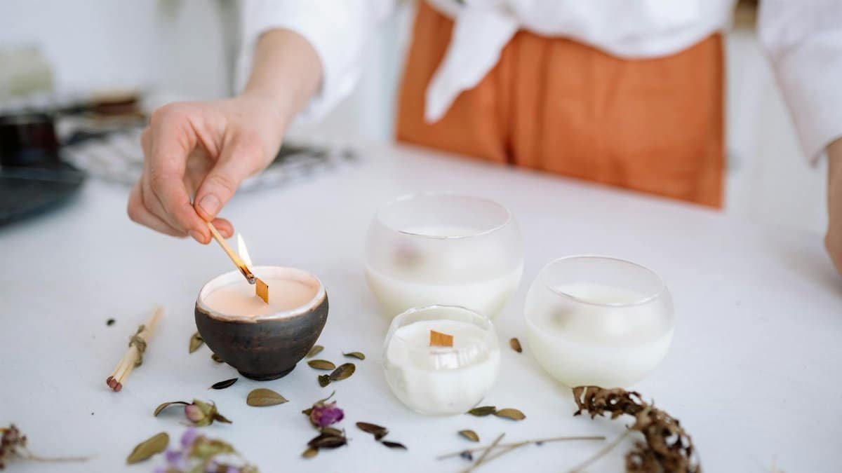 A hand lights a decorative candle among flowers and herbs, creating a serene ambiance.