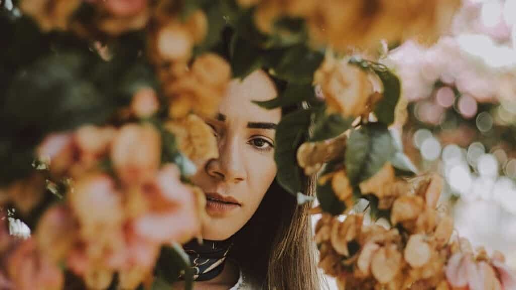 A beautiful woman partially hidden by colorful blooms captures a serene autumn moment.
