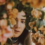 A beautiful woman partially hidden by colorful blooms captures a serene autumn moment.