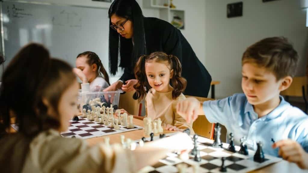 Kids engaging in a chess game with teacher guidance in a classroom.