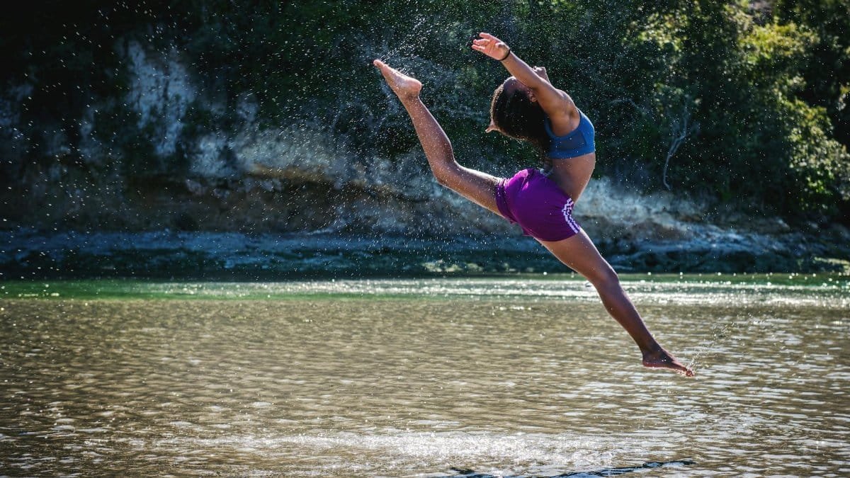 Young woman leaps in front of a river, showcasing flexibility and energy.