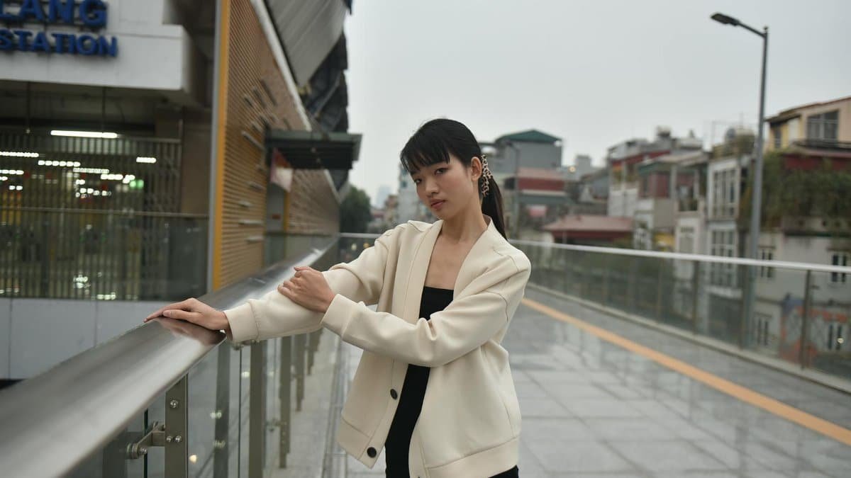 Young woman in stylish attire stands on an urban glass bridge, exuding modern elegance.