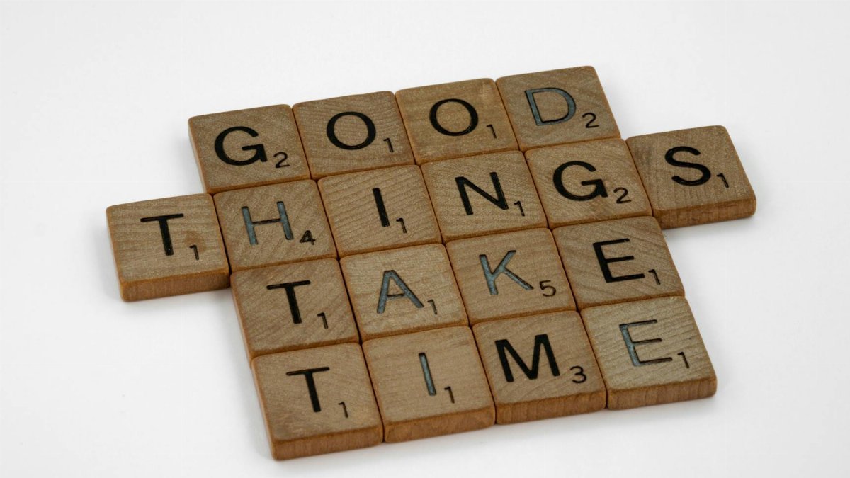 Close-up of wooden tiles spelling 'Good Things Take Time' on a white background.