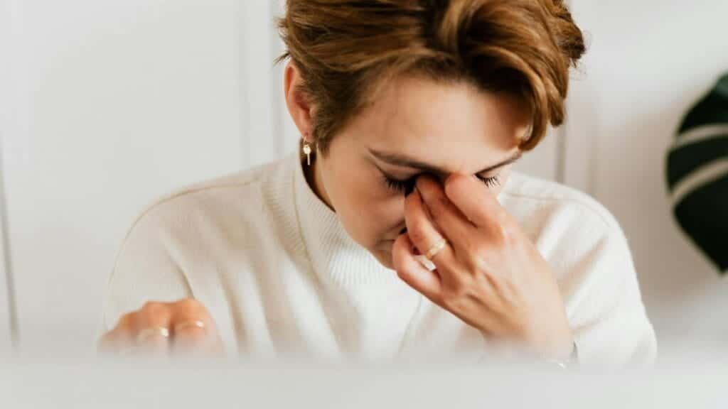 A close-up shot of a woman rubbing her eyes, conveying stress and fatigue indoors.