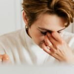 A close-up shot of a woman rubbing her eyes, conveying stress and fatigue indoors.