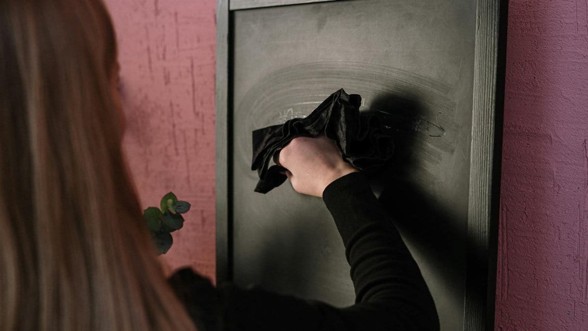 A woman using a cloth to erase a black chalkboard in an indoor setting.