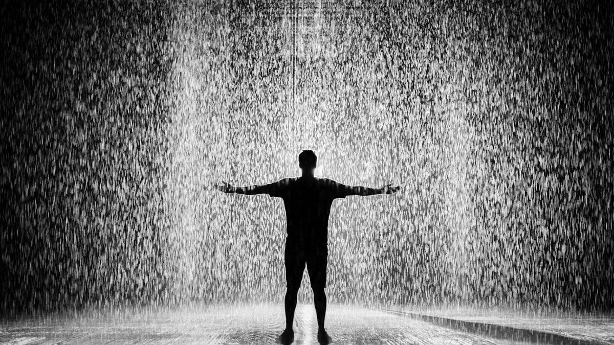A person joyfully standing in the rain with arms wide open in a dramatic black and white scene.
