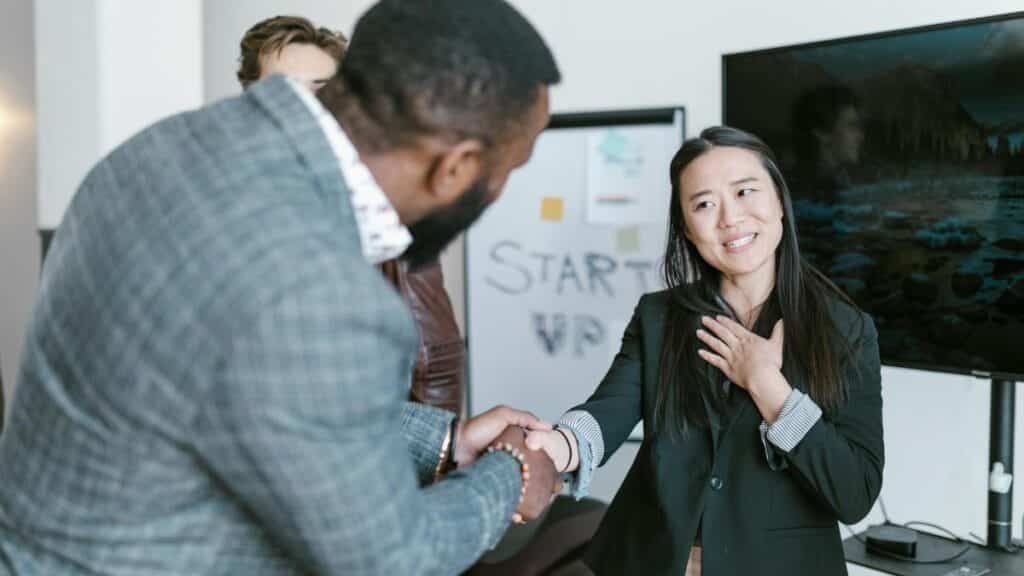 A diverse business team in formal attire exchanging a handshake in a modern office setting, signifying cooperation.