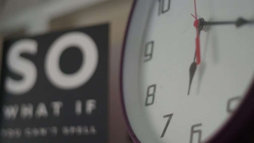 An analog wall clock showing time with a motivational sign partially visible in the background.