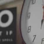 An analog wall clock showing time with a motivational sign partially visible in the background.