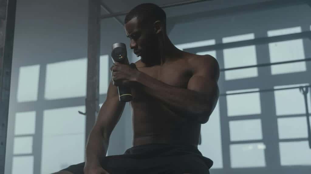 A dedicated athlete uses a massage gun to relax his muscles post-workout in the gym.