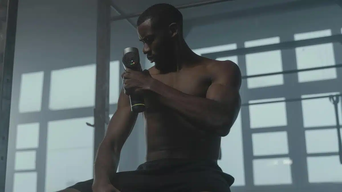A dedicated athlete uses a massage gun to relax his muscles post-workout in the gym.