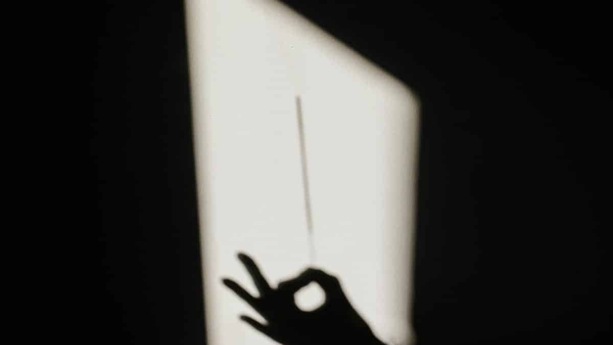 Silhouette of a hand casting an OK sign shadow on a wall, creating a dramatic light contrast.